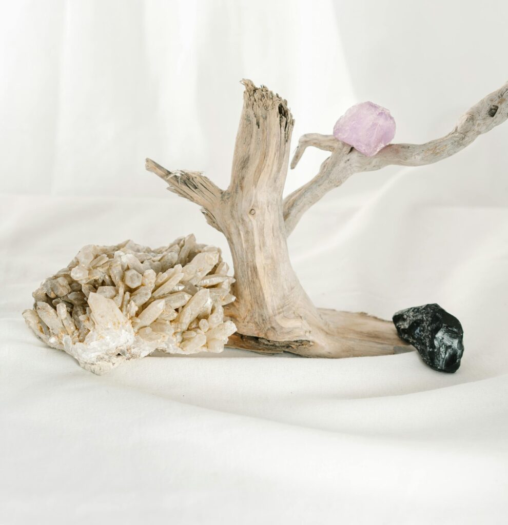Elegant arrangement of crystals and driftwood against a white backdrop, creating a serene and mystical ambiance.